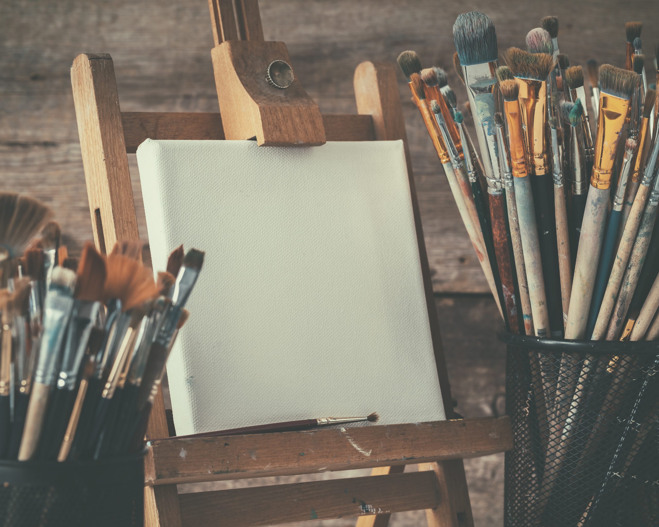Artistic equipment: empty artist canvas on easel and paint brushes in a artist studio. Retro toned photo.